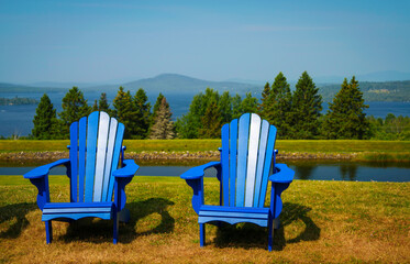 Two blue Cape Cod benches, or androidlike wooden chairs on a green hilltop overlooking Rangeley...