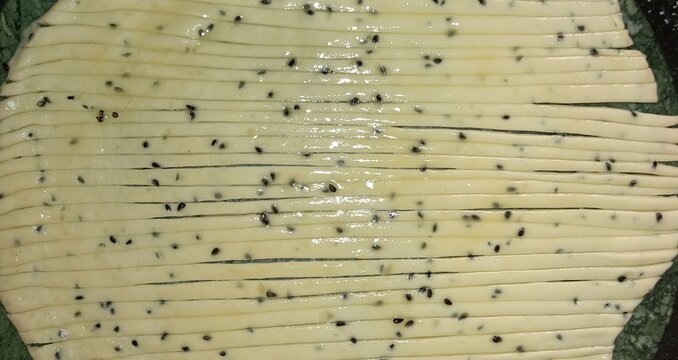 Kerala parotta (porotta) preparation. Dough glistening with oil and black sesame is flattened, cut in thin strips to be rolled spirally before pan-frying for signature flaky layered soft bread texture