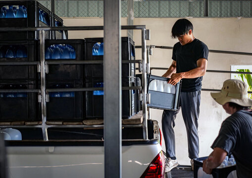 male warehouse worker lifting a bottled drinking water in a crate Load drinking water onto the delivery truck in waterdrink factory, small business