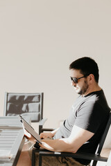 Man sitting on patio with sunglasses reading from an electronic tablet or book