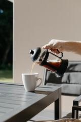 Man pouring filter coffee from a french press into a white cup at an outdoor table