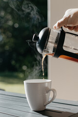 Man pouring filter coffee from a french press into a white cup at an outdoor table