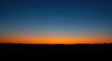 Obraz premium Scenic orange sunset over silhouetted trees at dusk, gradient sky