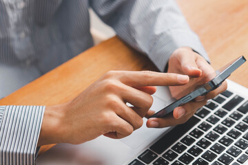 Businessman using laptop and smartphone in modern office, typing email, reading company policy...