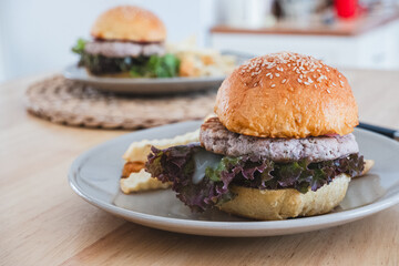 Two delicious plant-based burgers with lettuce and fries on plates, served on a wooden table. Comfort Food.