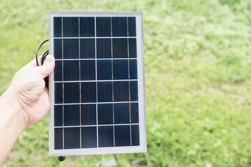 A hand holding a small portable solar panel against a blurred green outdoor background, symbolizing renewable clean energy concept.