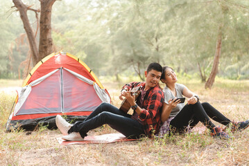 Young couple relaxing and playing guitar outside their tent during a peaceful camping trip, outdoor...