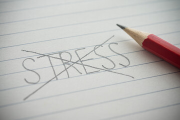 Close up pencil handwriting strikethrough STRESS word on notepad background. Not stressed, stress...