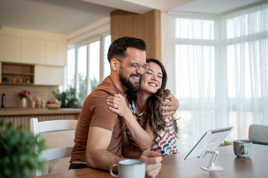 Happy couple embracing while video calling family on tablet at home