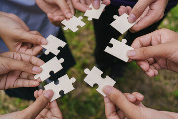Hands holding puzzle pieces against nature background, symbolizing teamwork, connection, and...