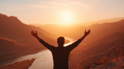 A man with outstretched arms facing the sunrise or sunset over distant mountains and a river, feeling freedom and happiness.