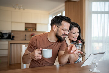 Happy couple using tablet and drinking coffee in kitchen