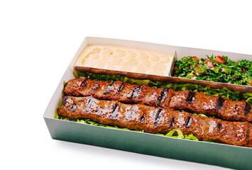 Grilled kebabs served with fresh salad and tahini in a takeout box