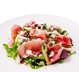Fresh salad with prosciutto, apple, and seeds served on a white plate