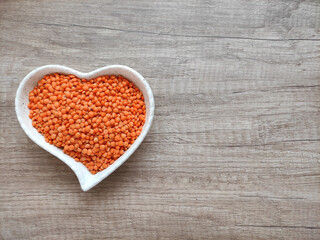 Dried small red lentils in a decorative plate on a wooden background