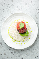 Stuffed red bell pepper on creamy risotto, garnished with spinach and herb oil, served on a white plate over a speckled grey background
