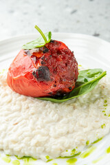 Stuffed red bell pepper on creamy risotto, garnished with spinach and herb oil, served on a white plate over a speckled grey background