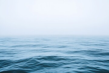 Fototapeta premium Vast open ocean with smooth waves, misty atmosphere, horizon line softly fading into white background.