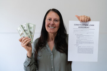 Happy woman smiling at camera and holding cash after taking a construction loan. Concept of loan...