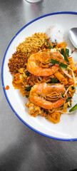 Pad Thai with fresh shrimp in a white plate with blue edges on a stainless steel table.