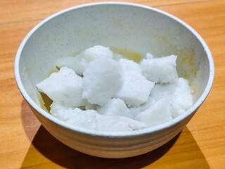 Pieces of lontong served in a white bowl, placed on a wooden table.