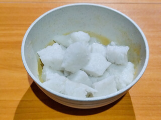 Pieces of lontong served in a white bowl, placed on a wooden table.