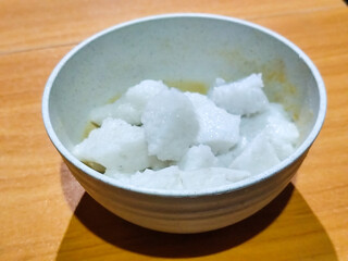 Pieces of lontong served in a white bowl, placed on a wooden table.