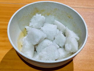 Pieces of lontong served in a white bowl, placed on a wooden table.