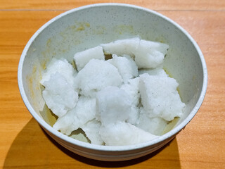 Pieces of lontong served in a white bowl, placed on a wooden table.