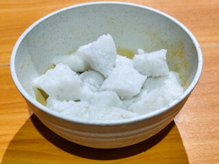 Pieces of lontong served in a white bowl, placed on a wooden table.
