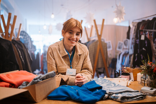 Smiling Sales Associate at Trendy Clothing Store with Colorful Apparel