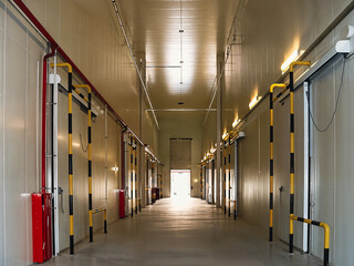 A bright, long industrial hallway with a series of doors and safety barriers.