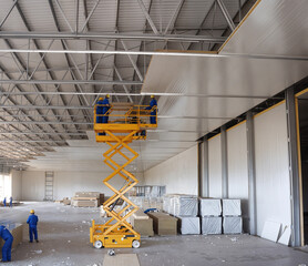 Inside a warehouse, construction workers are installing ceiling panels, teamwork at work.
