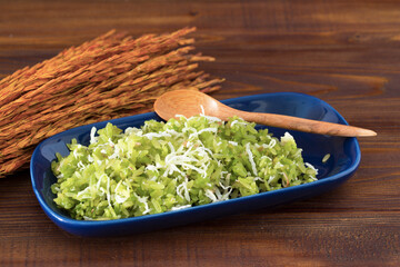 Thai dessert pounded unripe rice with shredded coconut on wood table.