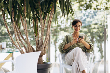 Young woman sitting on a chair under palm trees and talking on the phone