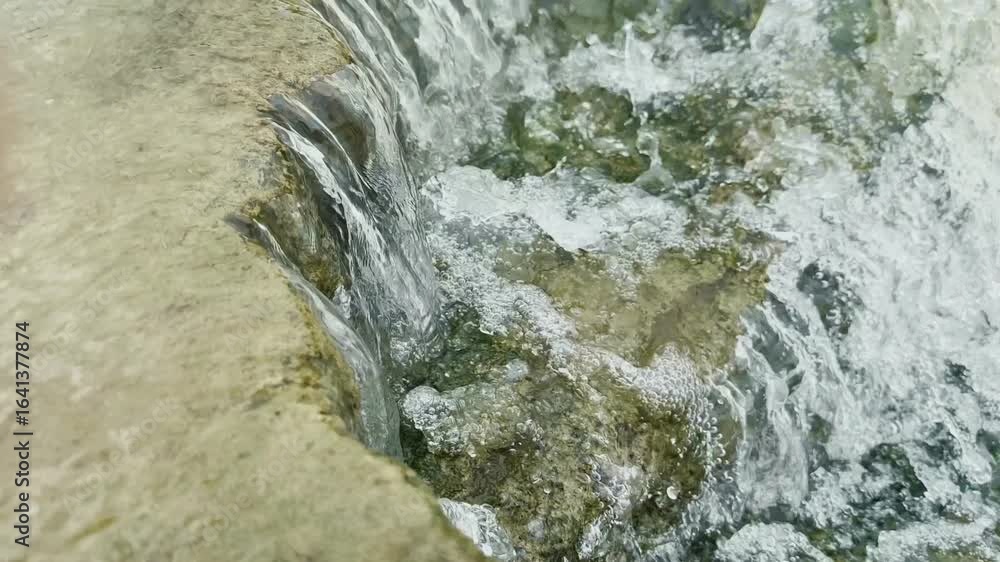 Poster a close-up dynamic view of water flowing and cascading over a series of textured moss-covered surfac
