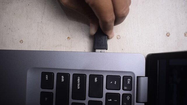 Close up of a woman's hand plugging a USB cable into a port on a laptop