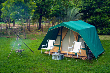 Camping tents on the green grass, background with many big trees, vintage cabin tents, antique oil lamps, retro chairs