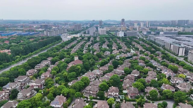 4K aerial drone footage showcasing a modern residential neighborhood surrounded by lush greenery, tree-lined streets, and nearby urban skyline in the distance.