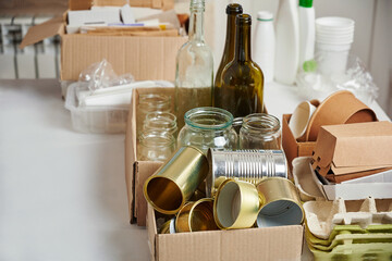 Sorting garbage for recycling. Cardboard boxes with various garbage, plastic and tin cans, glass bottles on table. Waste sorting, waste recycle. Garbage separation concept.