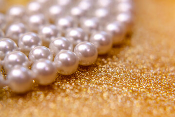 A necklace of pearls lies on a shiny gold background.
