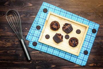 Top view of fresh homemade delicious vanila and chocolate muffins in paper cupcake holder with cookie and cream isolated on napkin, tablecloth on wooden background.
