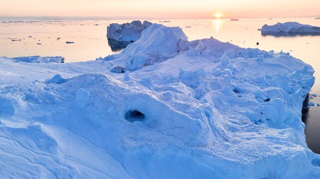 A tall melting iceberg in the Arctic Ocean. A glacier with a lake and waterfall. Clear ice floats in turquoise water. Ecology, melting ice, climate change, global warming. Aerial view. Midnight sun.