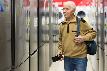 elderly man choosing refrigerator in showroom of electrical appliance store