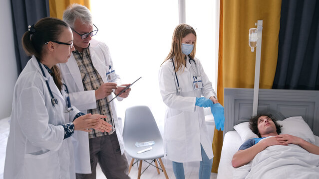 The doctor, the resident and the intern examine the young patient. The man lies in a hospital bed and answers questions from doctors