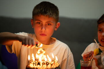 Celebrating a special moment with friends, a young boy carefully makes a wish while lighting the...