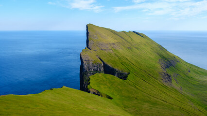 Majestic cliff by the ocean near the Faroe Islands with stunning green landscapes