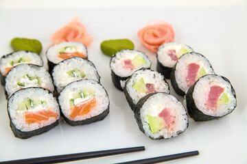 Fresh Sushi Rolls with Salmon, Tuna, Avocado, and Cream Cheese on White Plate with Wasabi, Pickled Ginger, and Chopsticks. Japanese Cuisine and Seafood Concept