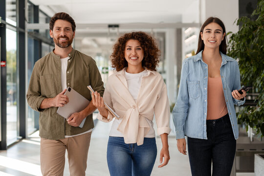 Smiling businesspeople walking together in office hallway - Powered by Adobe
