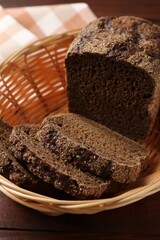 Pieces of fresh rye bread in wicker basket on wooden table, closeup